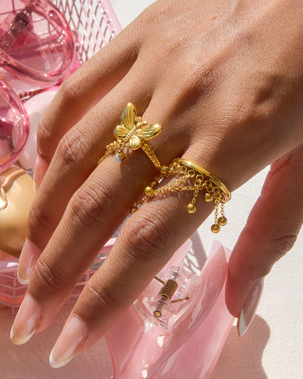 Hand wearing a gold ring with a butterfly design against a pink background