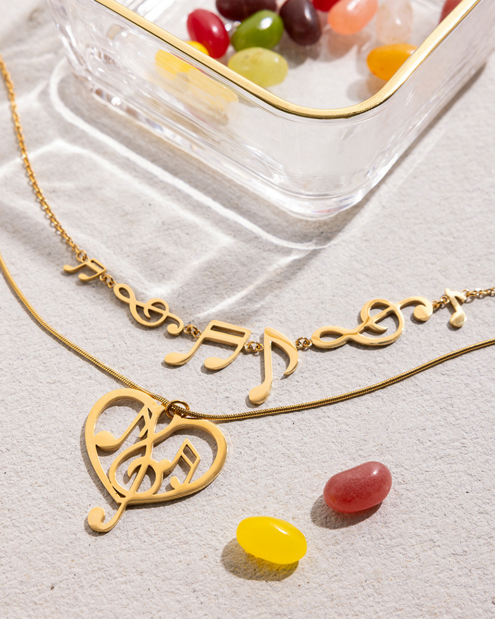 Gold necklace with musical note designs on a light gray surface with jelly beans.