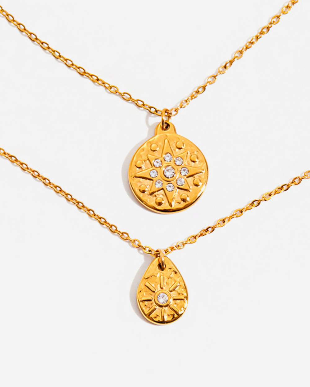 Two gold necklaces with circular and teardrop pendants on a white background