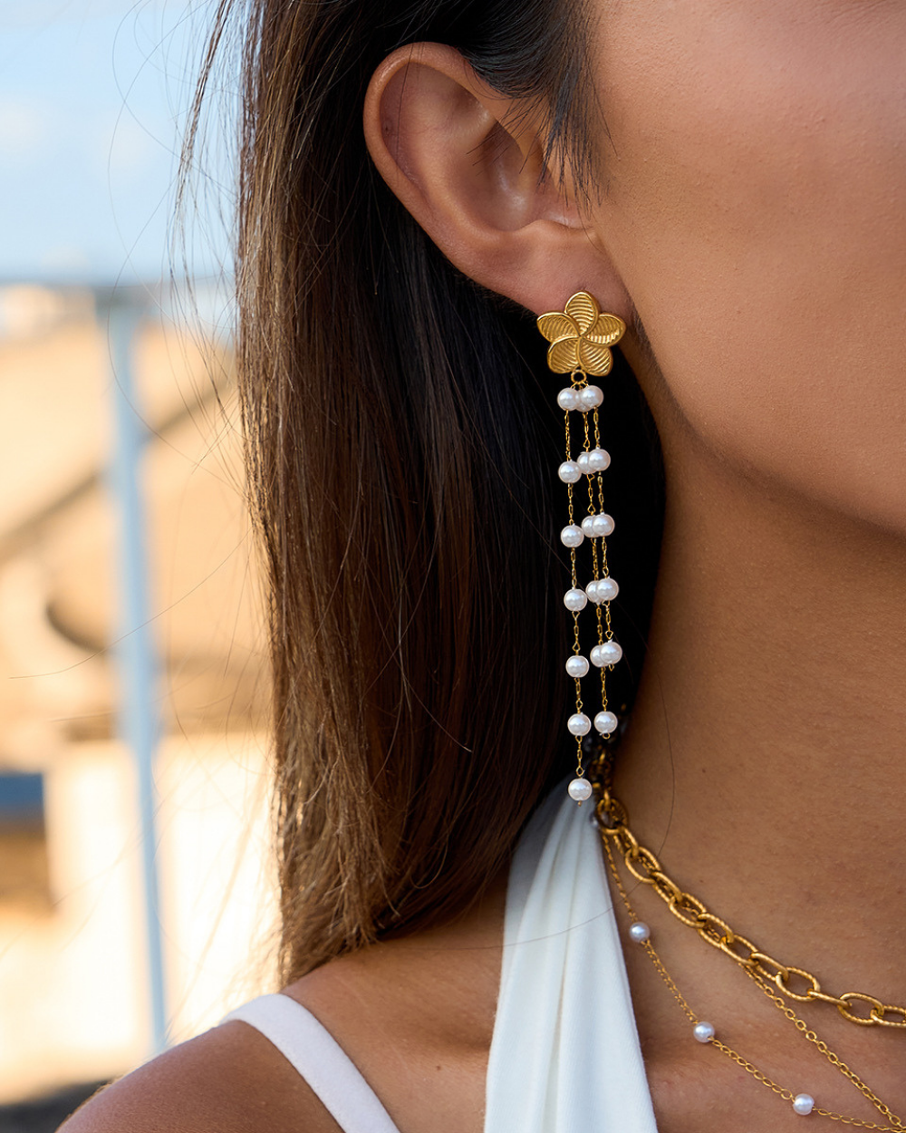Gold earrings with pearl strands worn by a person against a blurred outdoor background