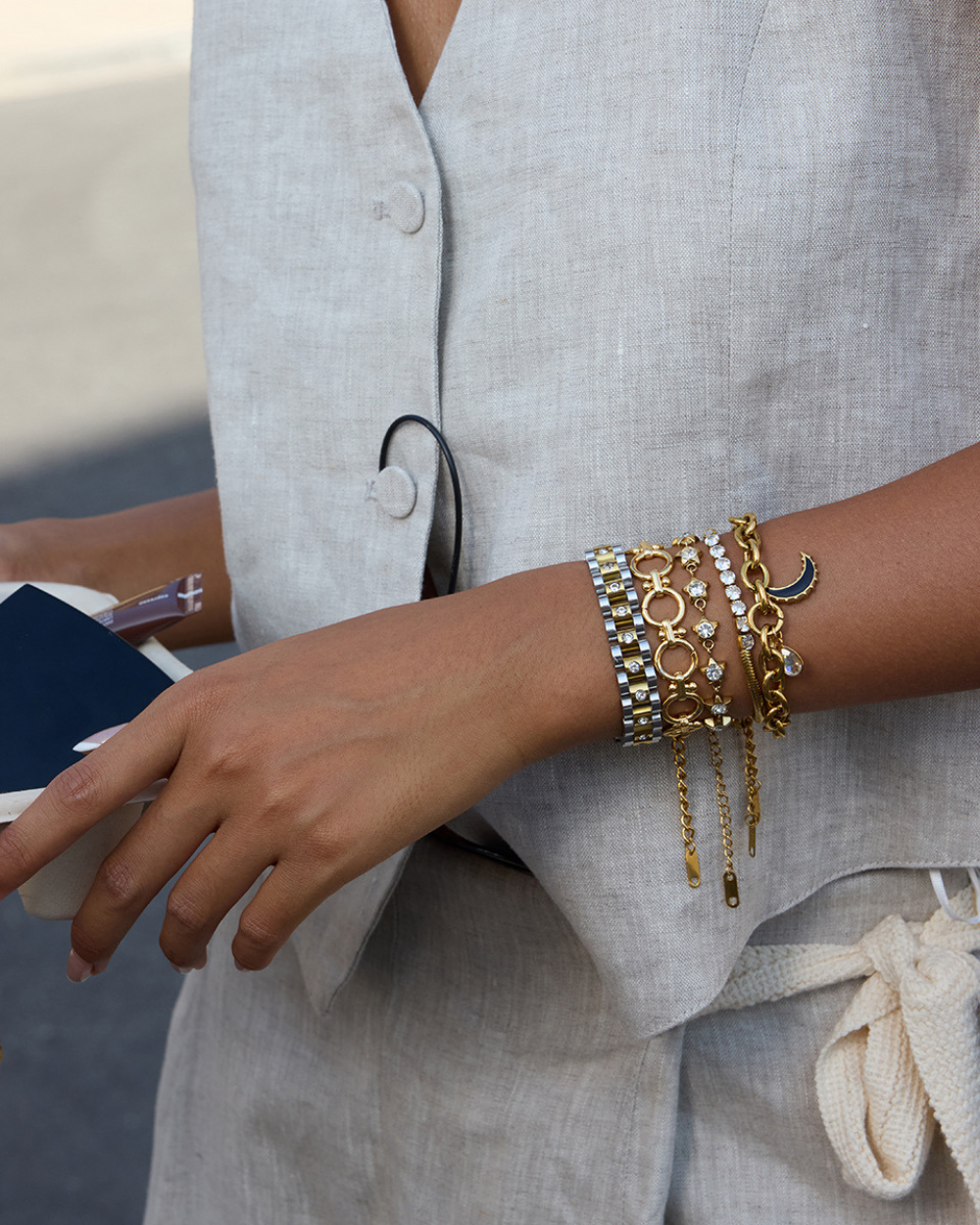 Close-up of a person wearing multiple gold bracelets on a light gray outfit.