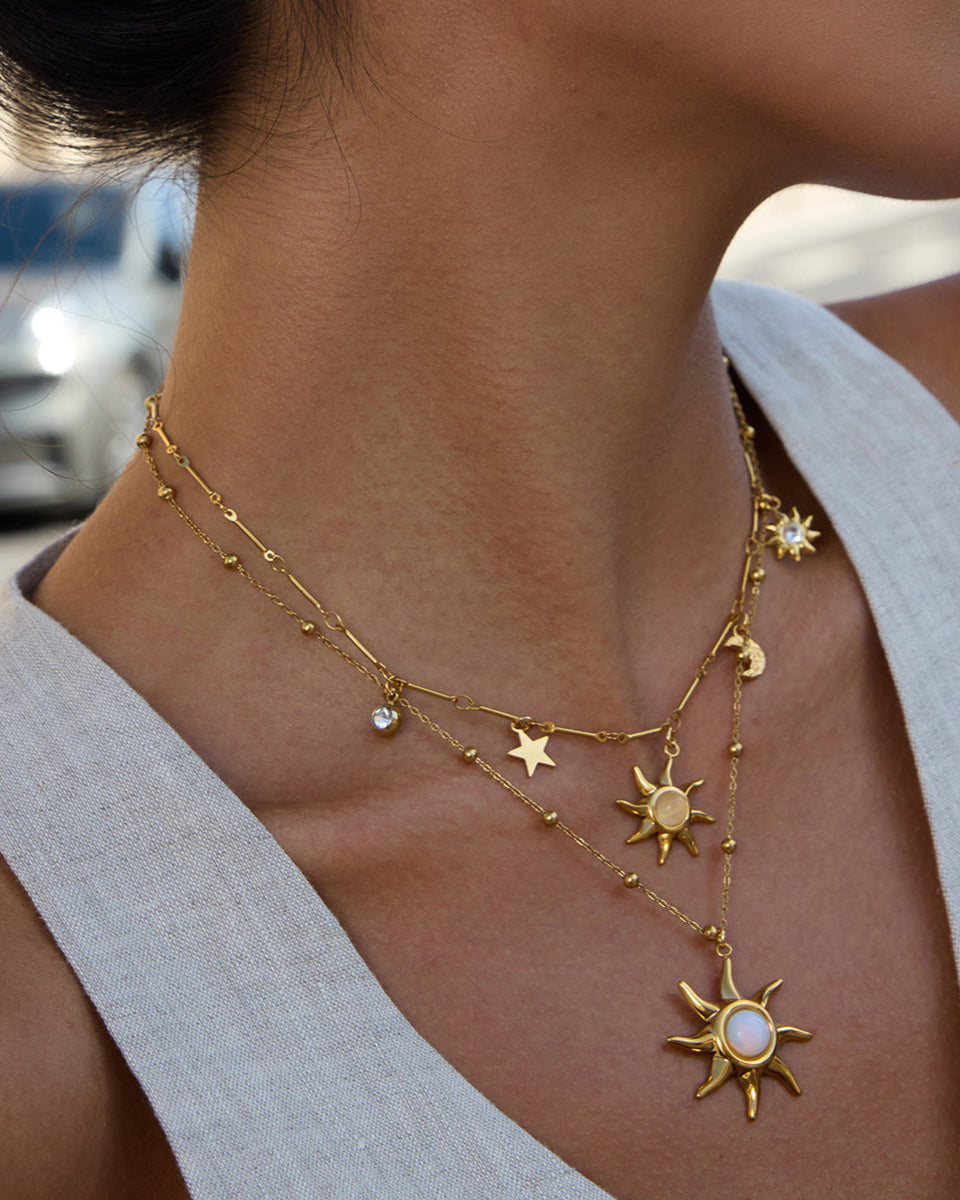 Gold necklace with star and sun pendants on a person wearing a light gray top.