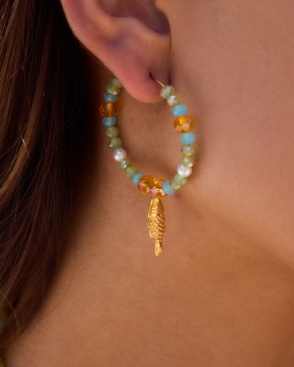 Beaded earring with a gold leaf charm worn by a person