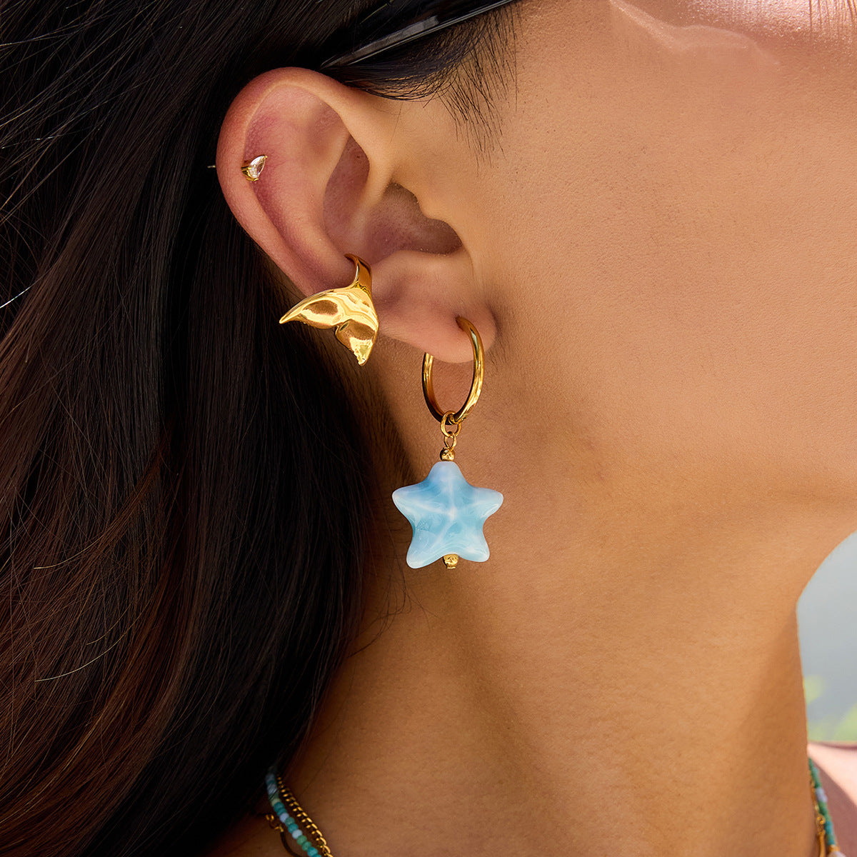 Close-up of an ear wearing a gold hoop earring with a blue star-shaped charm.