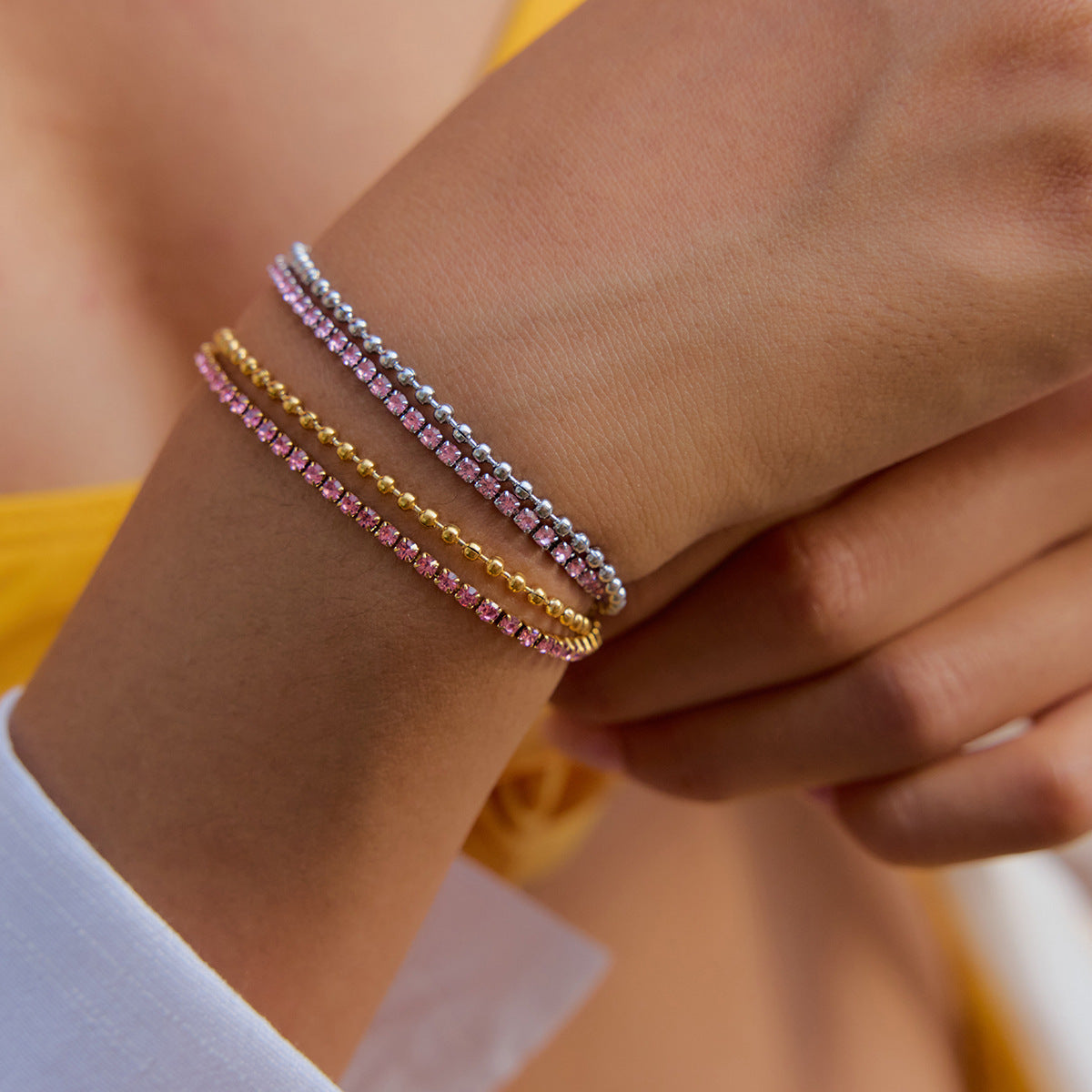 Model wearing layered gold and silver pink tennis bracelets with yellow top