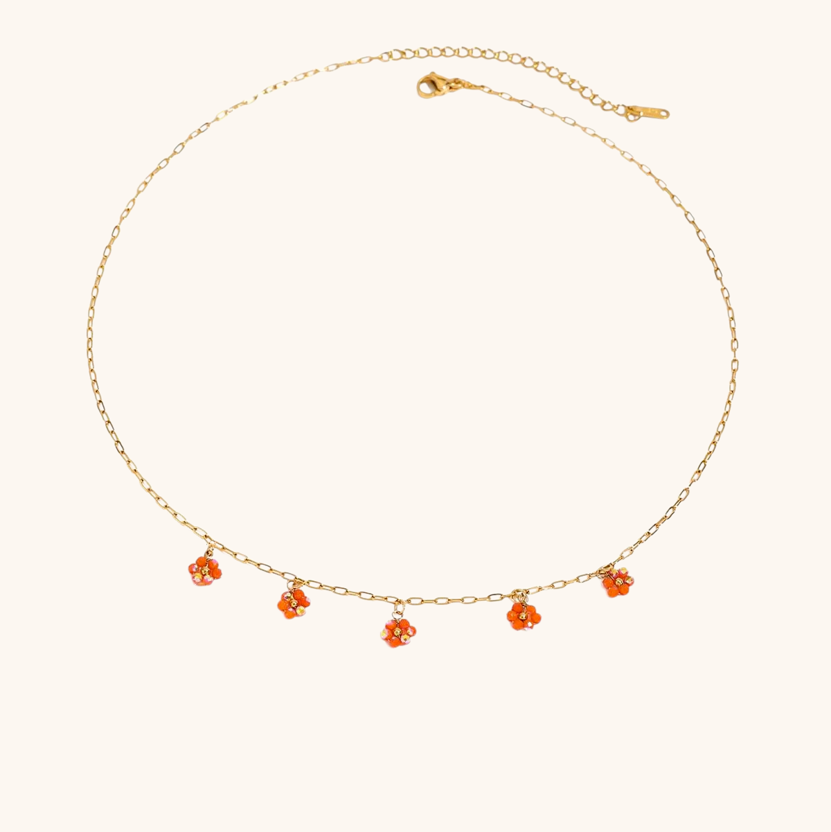 Delicate orange flower charm necklace with gold chain on floral background