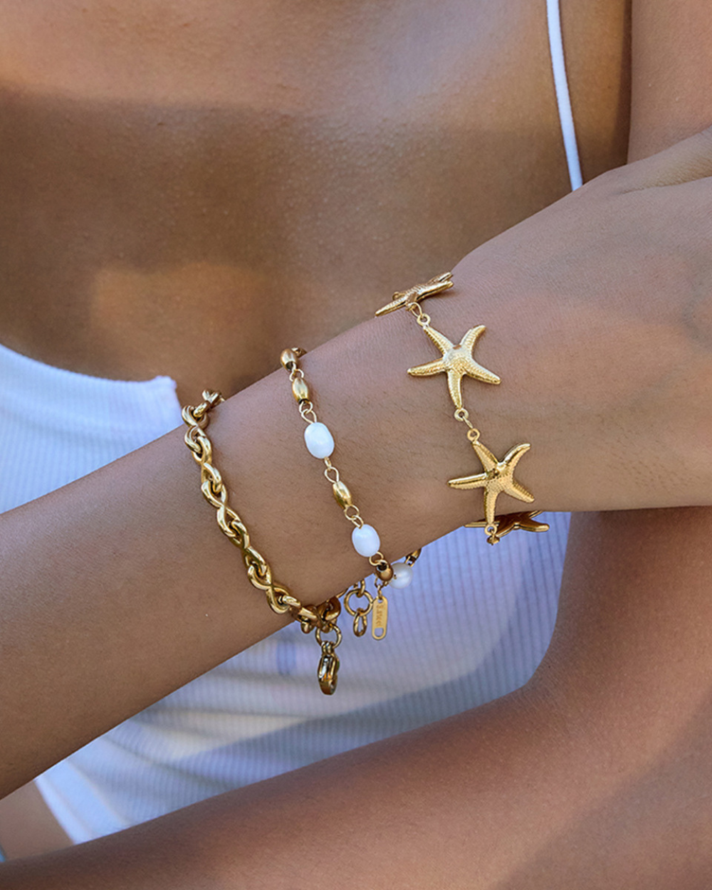 Gold bracelet with starfish charm on a wrist against a blurred background
