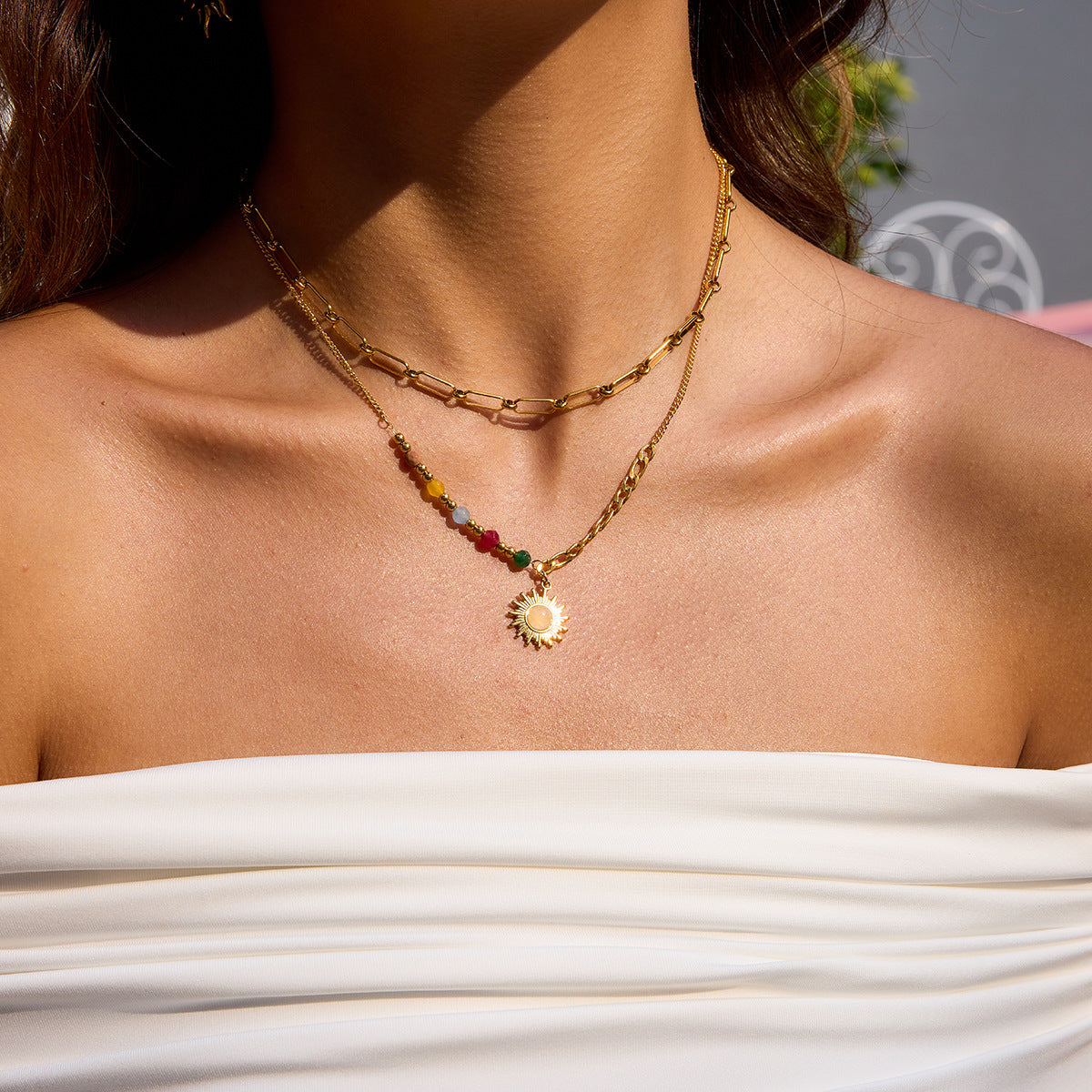 Layered gold paperclip chain necklace worn with a beaded sun pendant