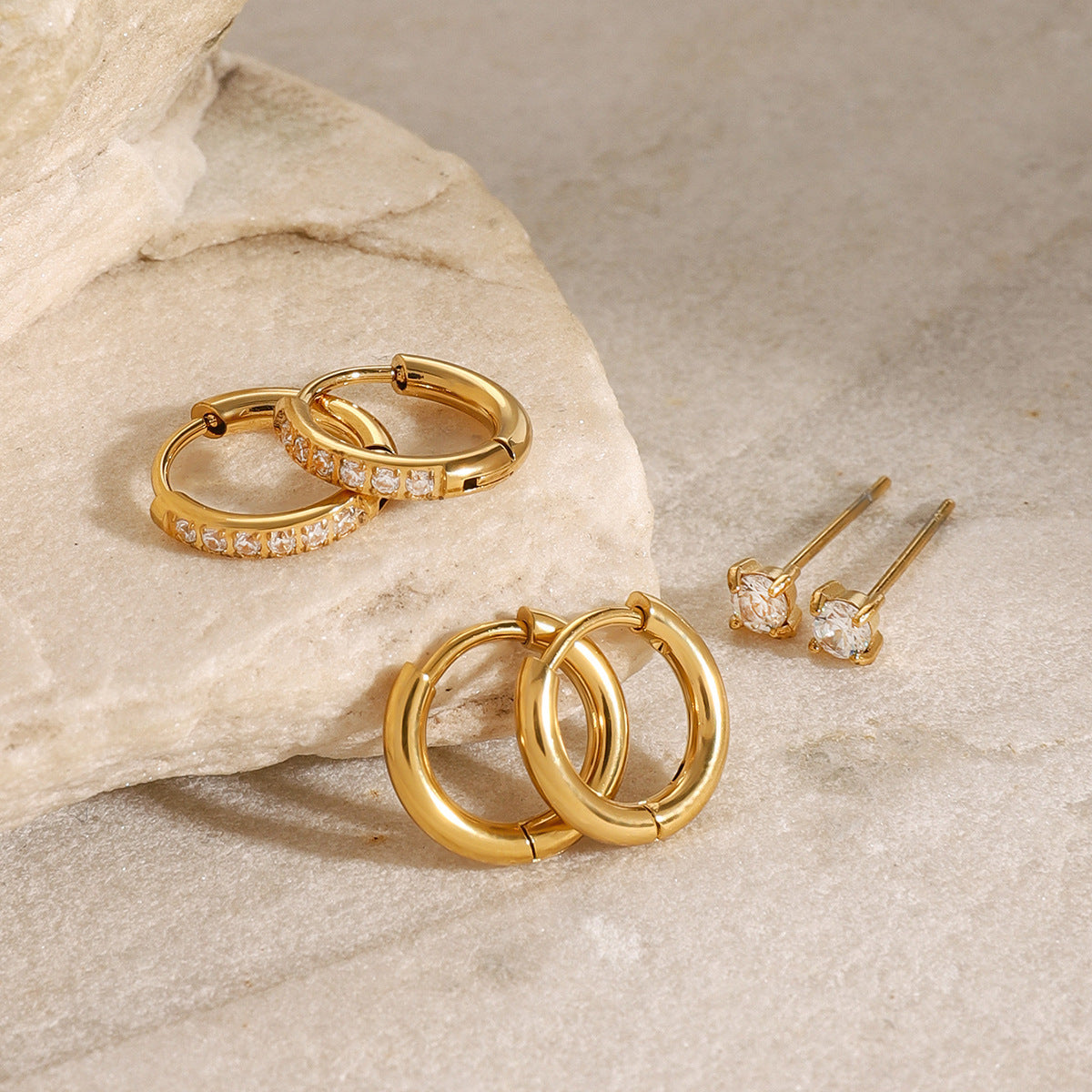 Round-cut cubic zirconia gold stud earrings, close-up detail on textured surface.