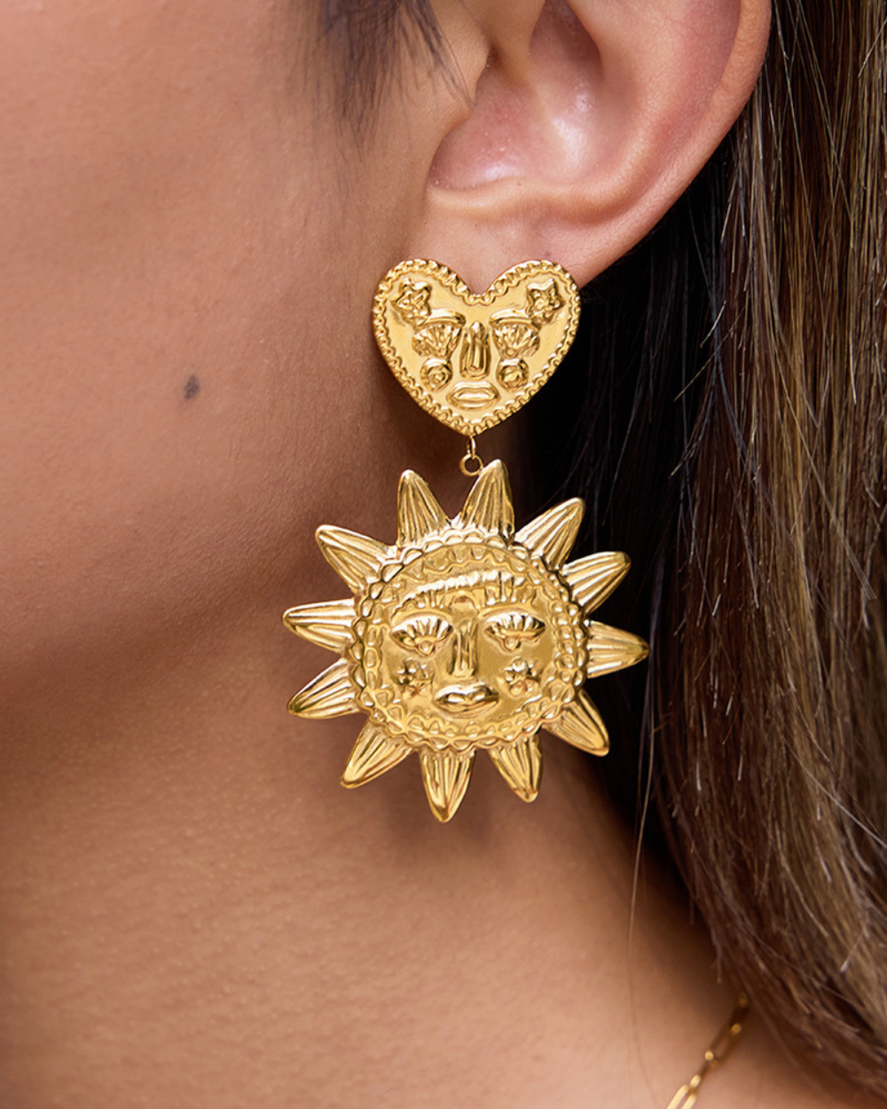 Gold sun-shaped earrings worn by a person