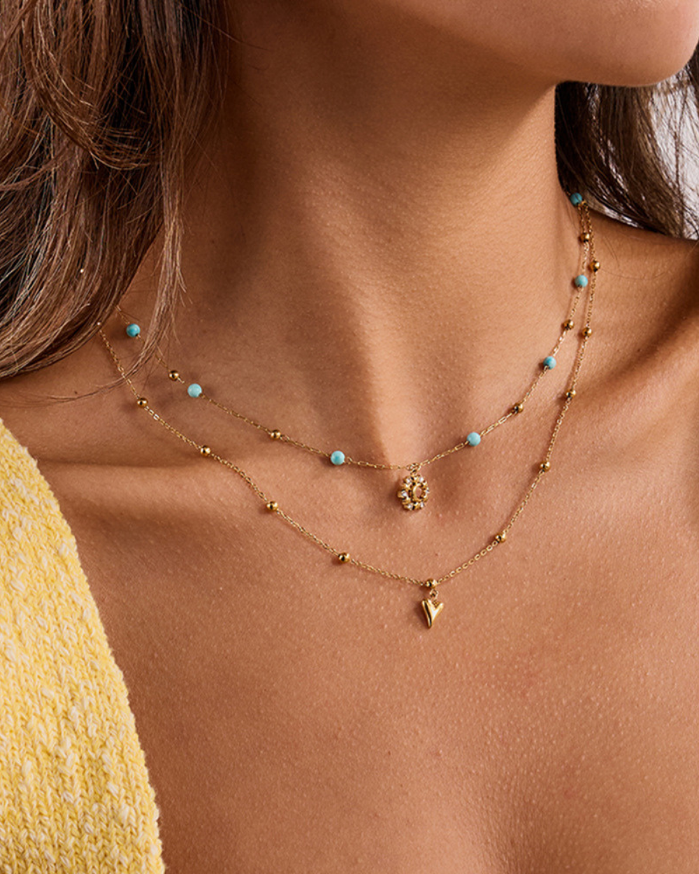 Close-up of a woman wearing a gold necklace with heart pendant and turquoise beads.
