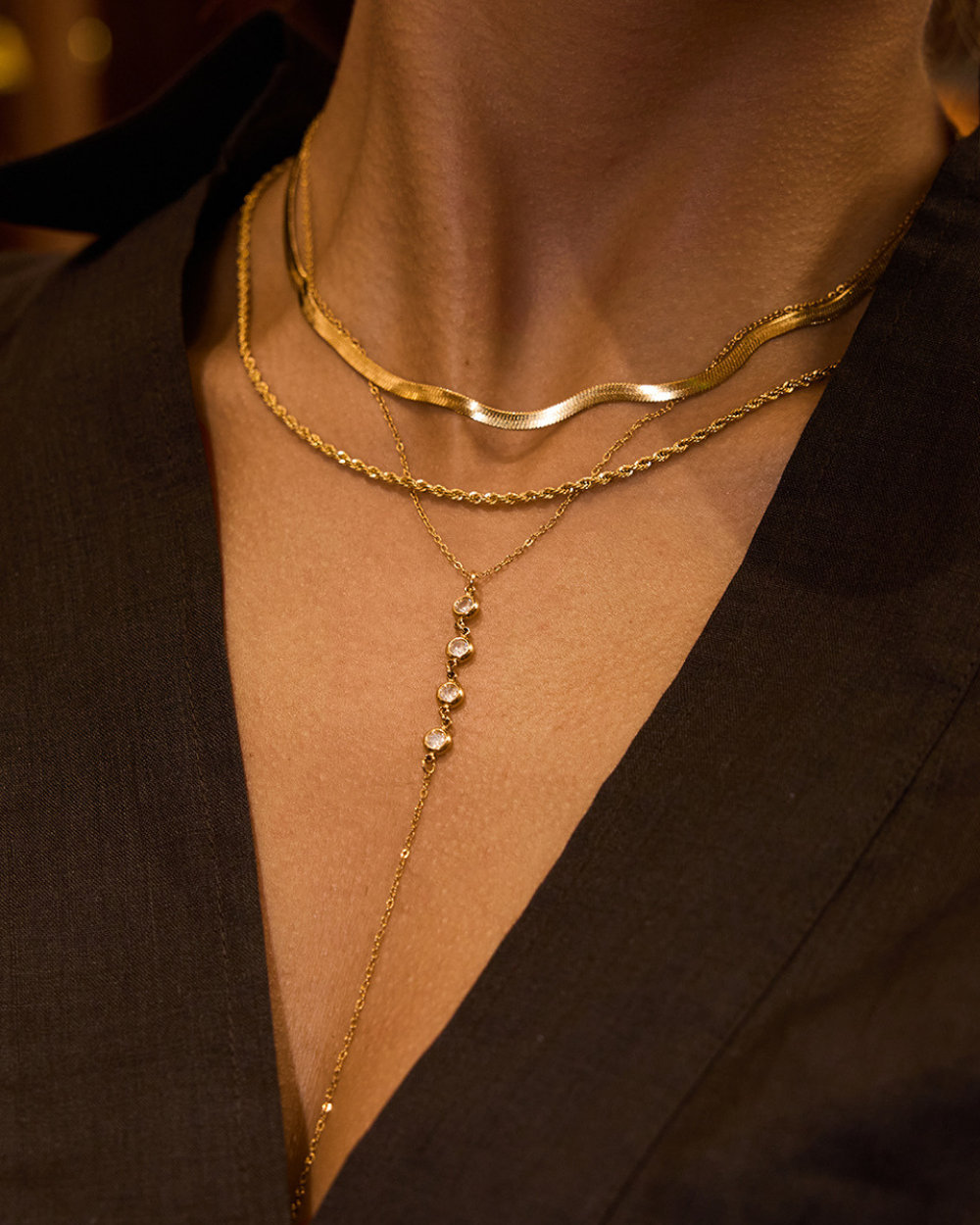Close-up of a person wearing two gold necklaces against a dark background