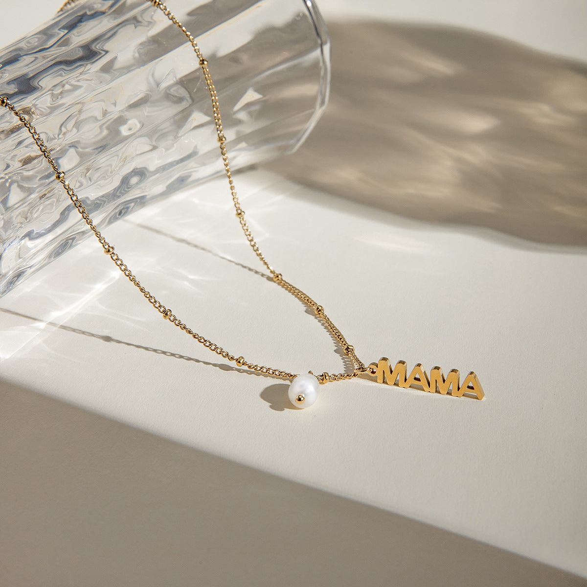 Gold chain necklace with vertical MAMA charm and pearl, styled on a marble background