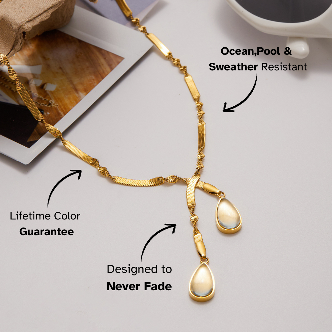 Gold necklace with teardrop pendants on a light gray surface, featuring text about its features.