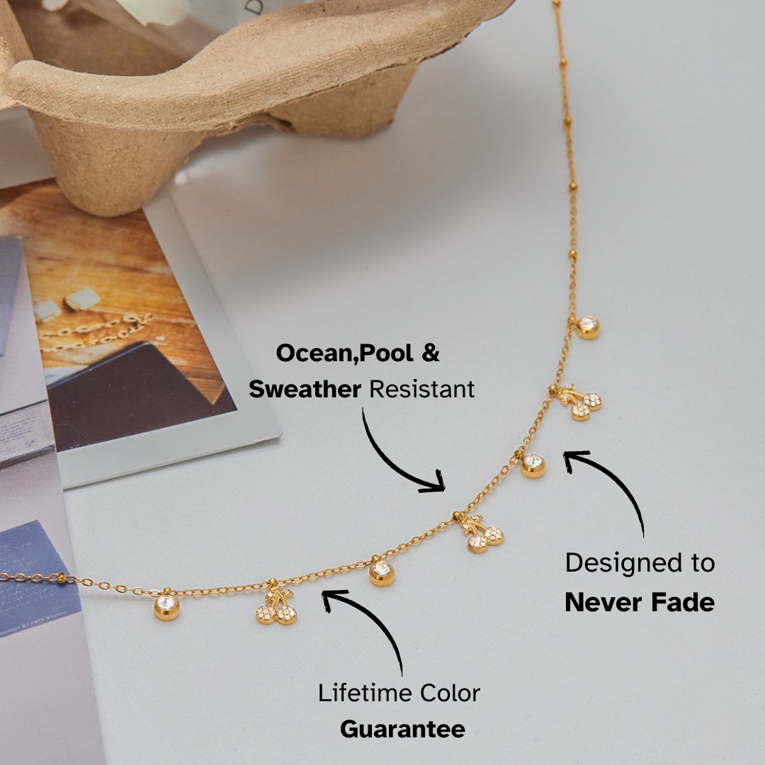 Flat lay of gold necklace with cherry and crystal charms styled on magazine background