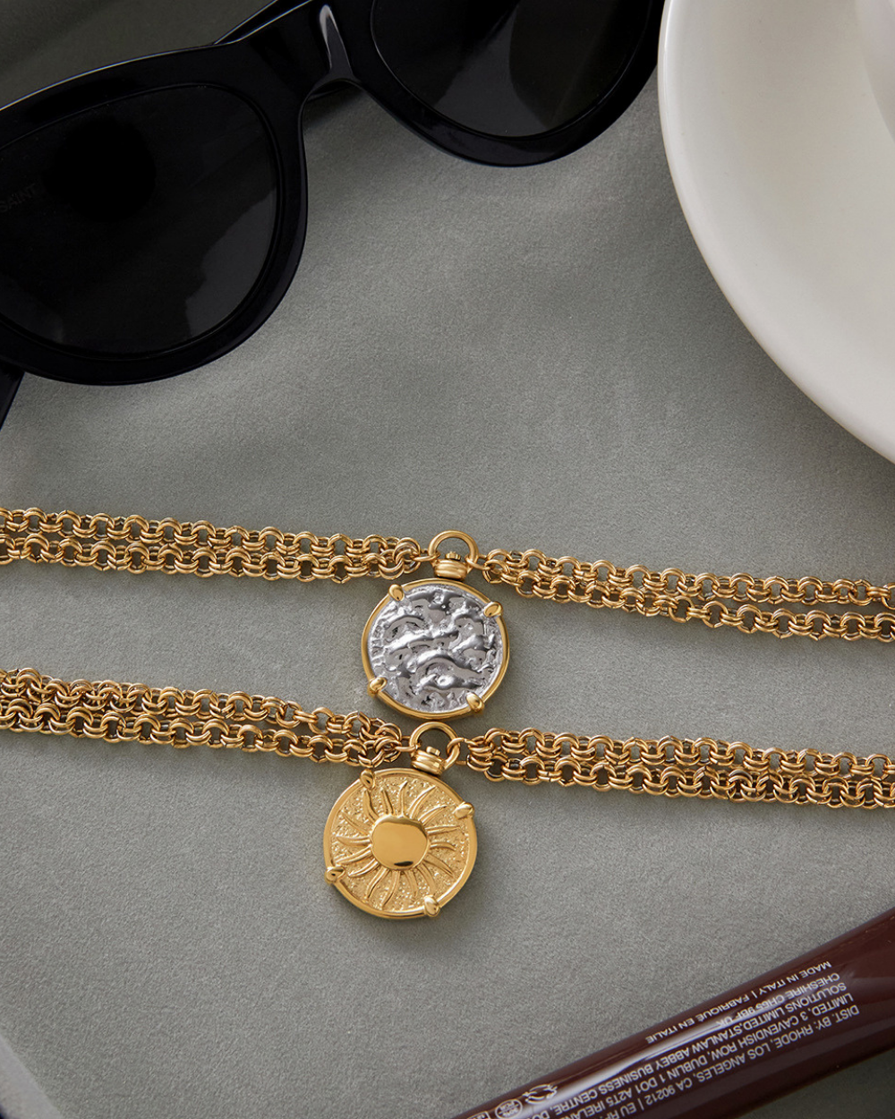 Two gold necklaces with pendants on a gray surface.