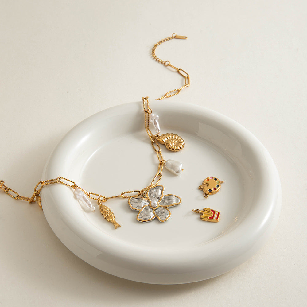 Close-up of necklace showing detailed gold fish, shell, and pearl charms with hammered metal flower