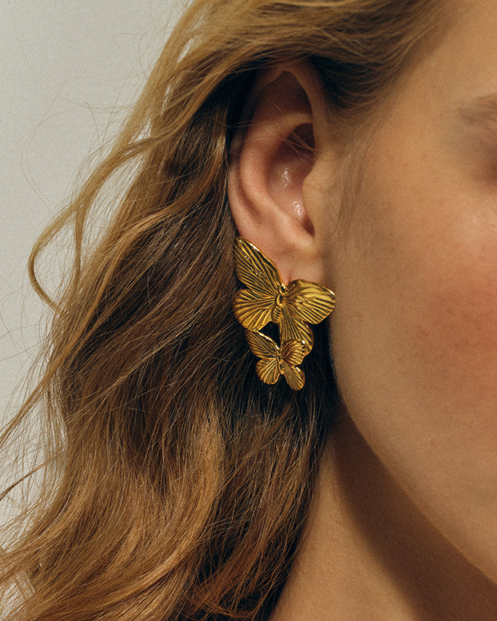 Gold butterfly earrings worn by a person with wavy hair.