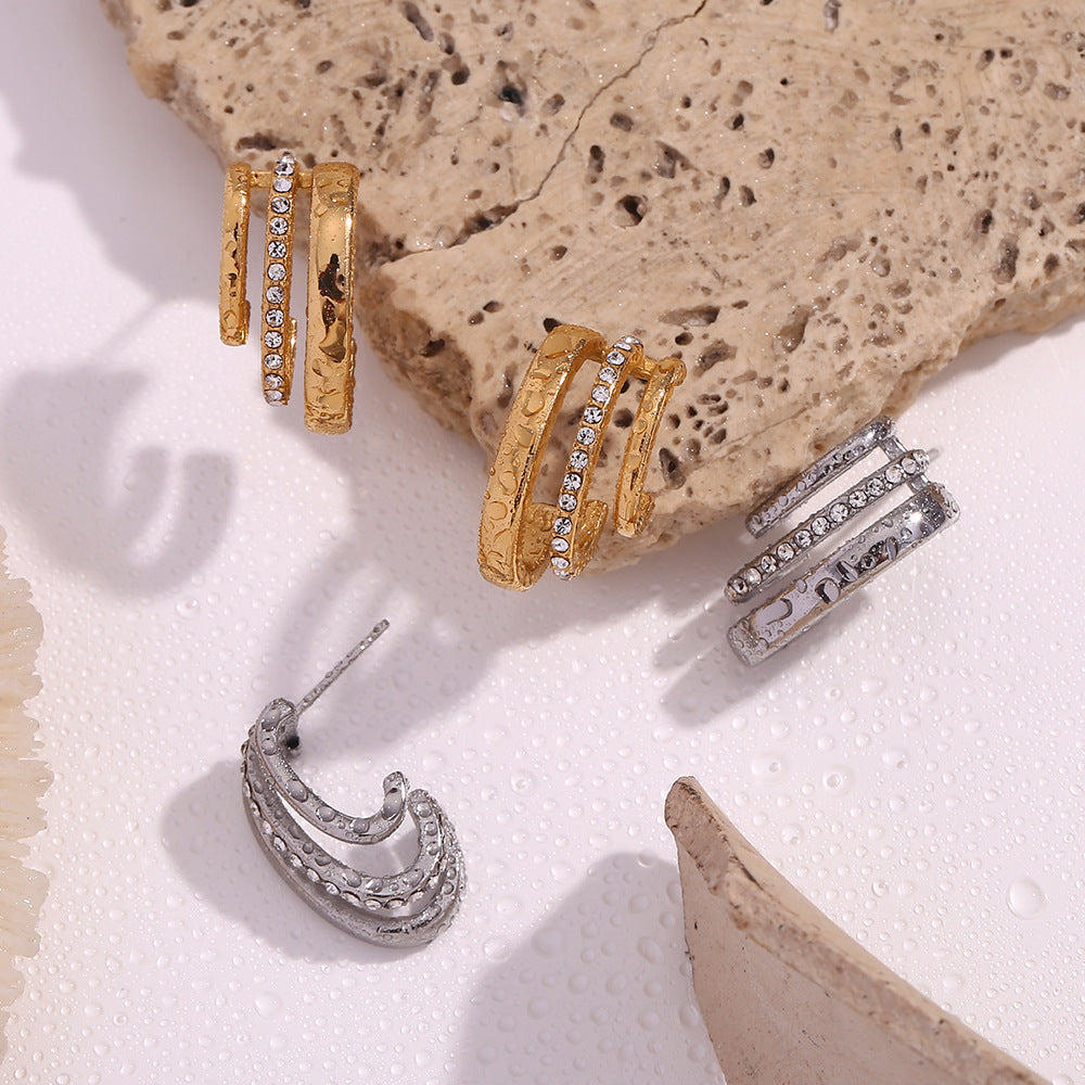 Gold and silver hoop earrings on a textured stone surface