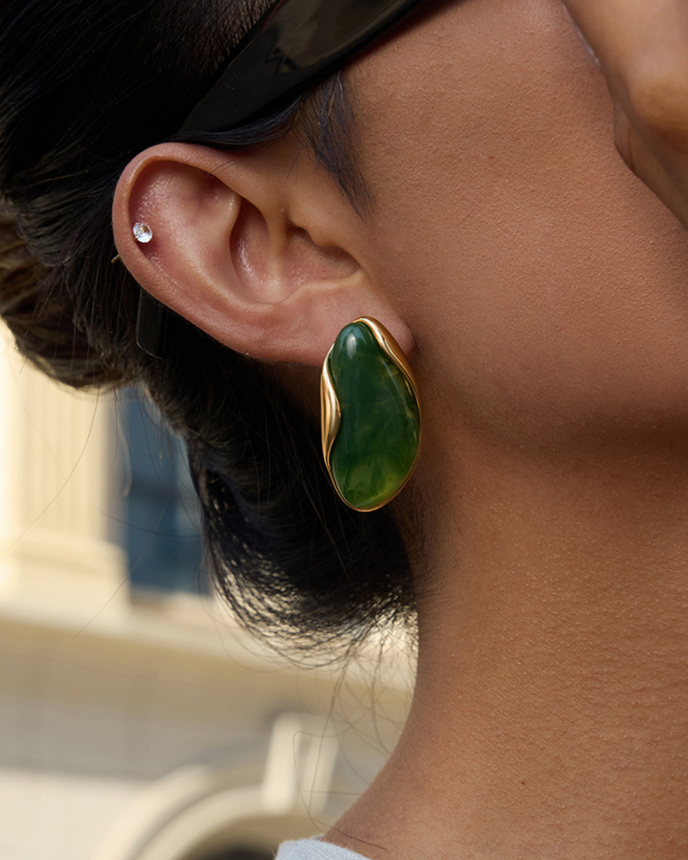 Close-up of a person wearing a gold earring with a green stone.