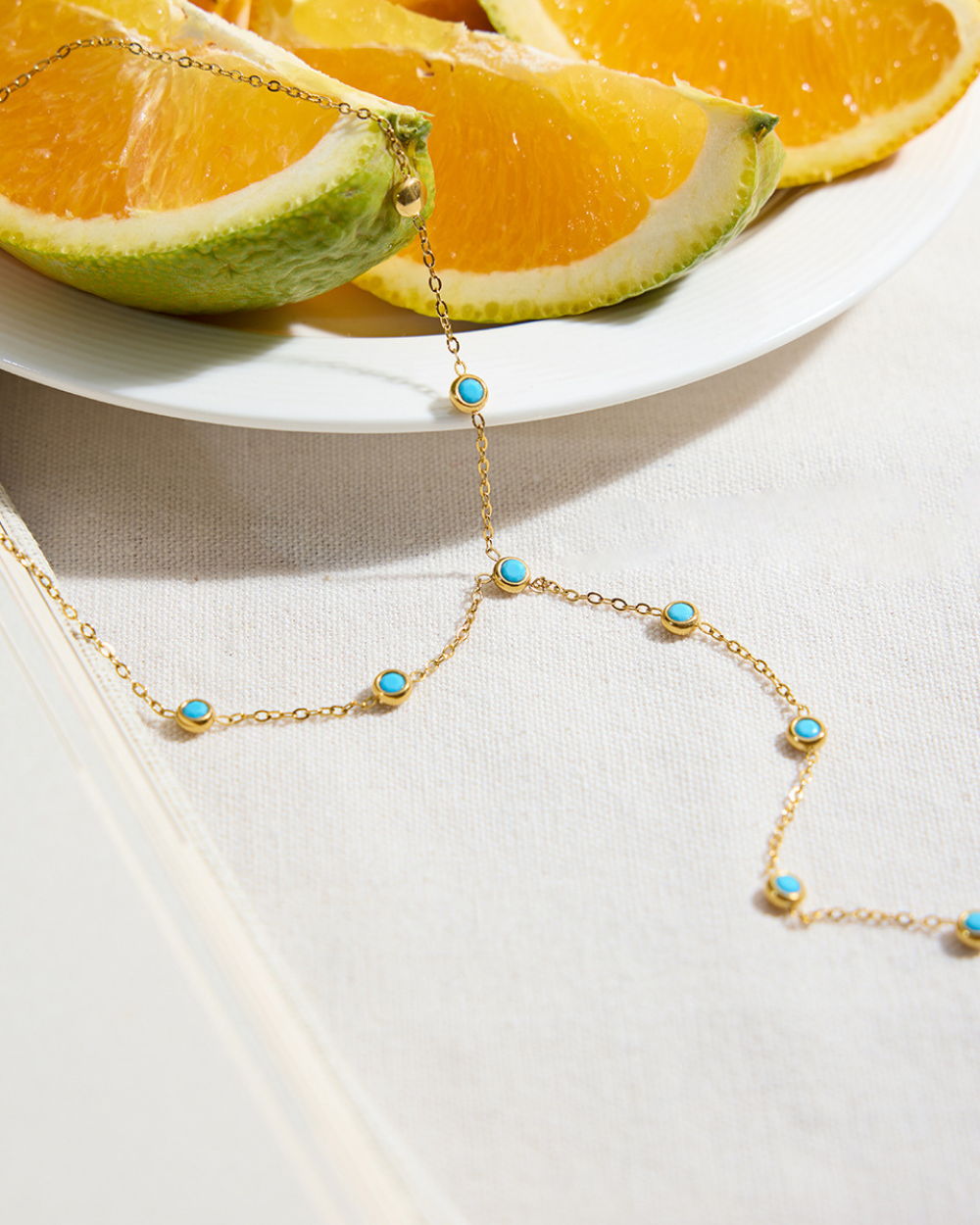 Gold necklace with turquoise stones on a white surface with orange slices in the background