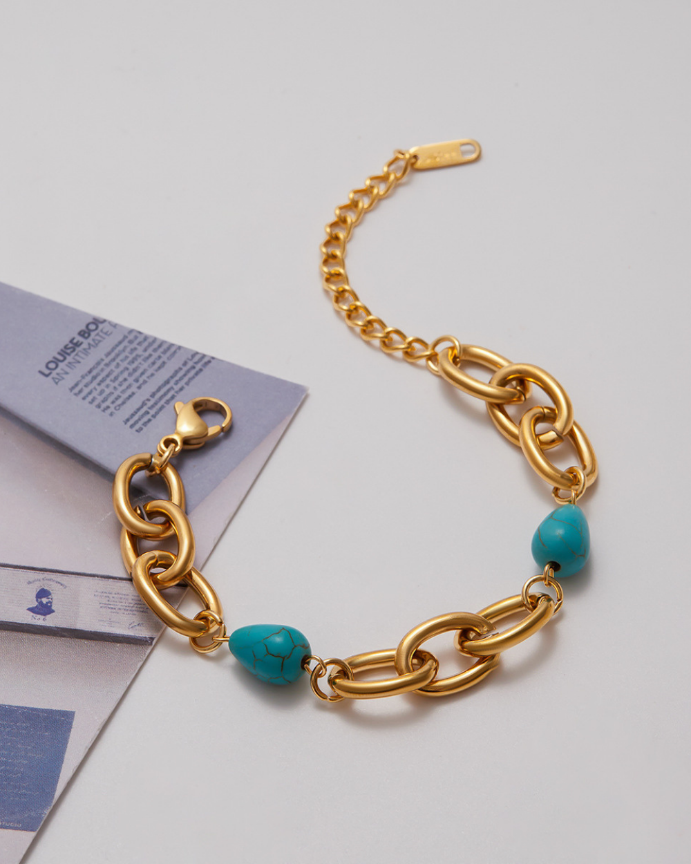 Gold chain bracelet with turquoise beads on a light gray background