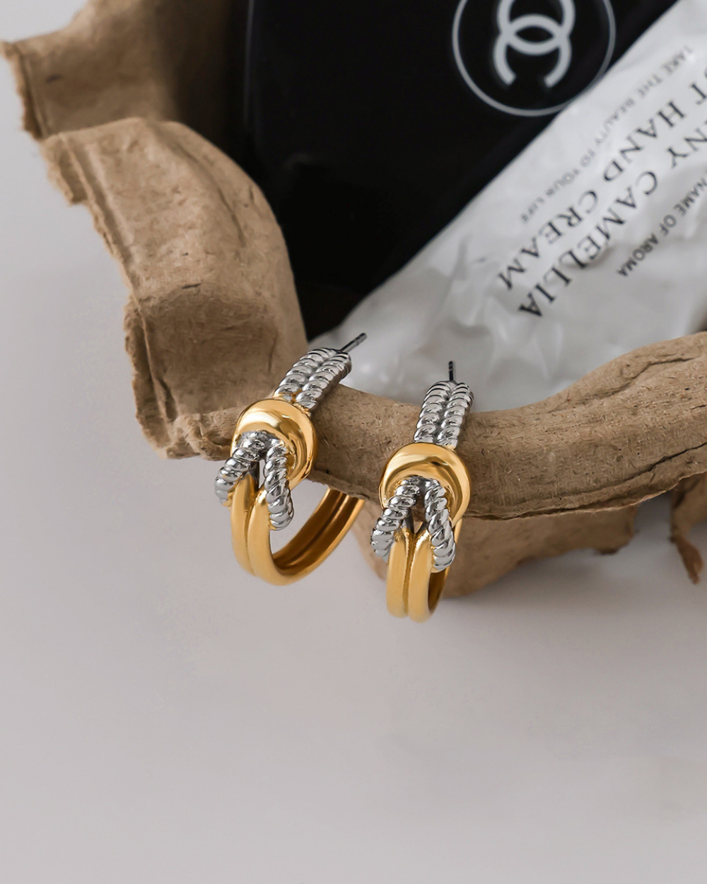 Gold and silver hoop earrings on a textured surface with a visible brand logo.