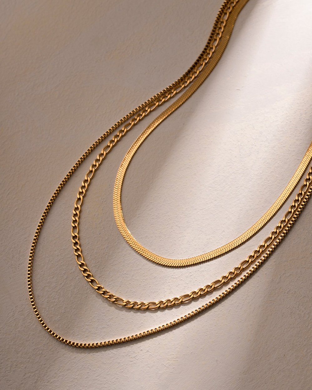 Two gold chains draped over a light brown surface