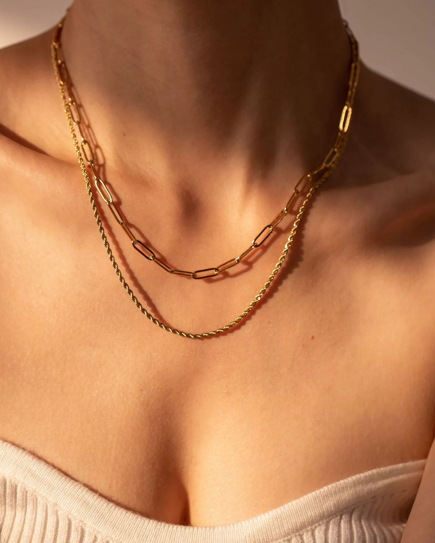 Close-up of a person wearing a gold chain necklace with a neutral background