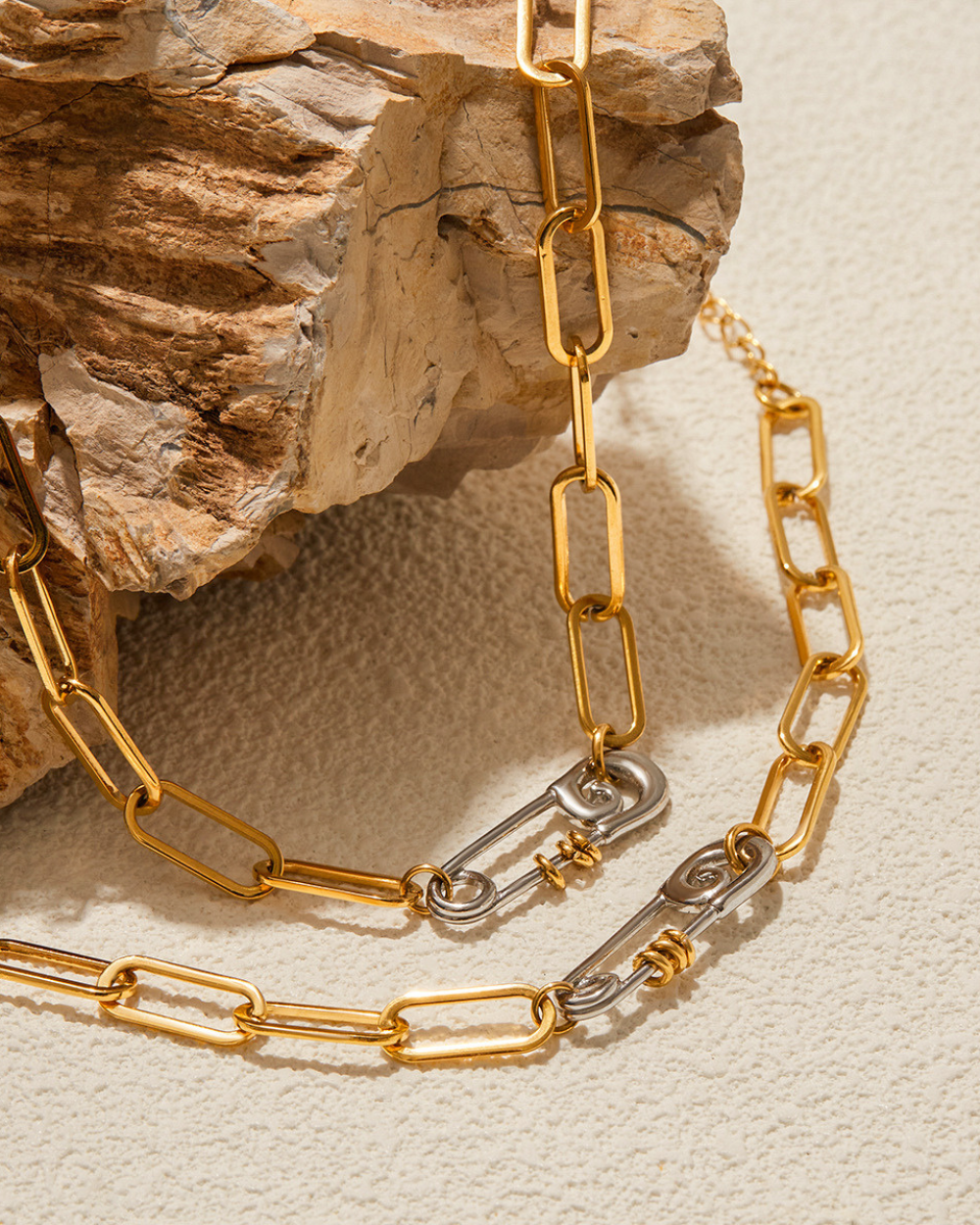 Gold chain necklace with a silver clasp on a textured beige surface