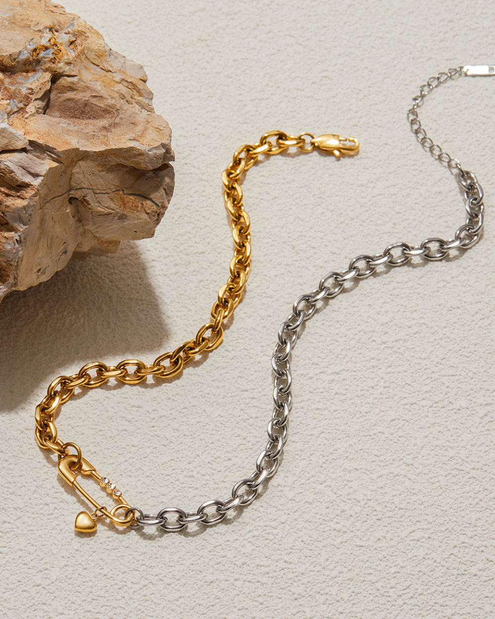 Gold and silver chain bracelets on a textured surface with a rock.
