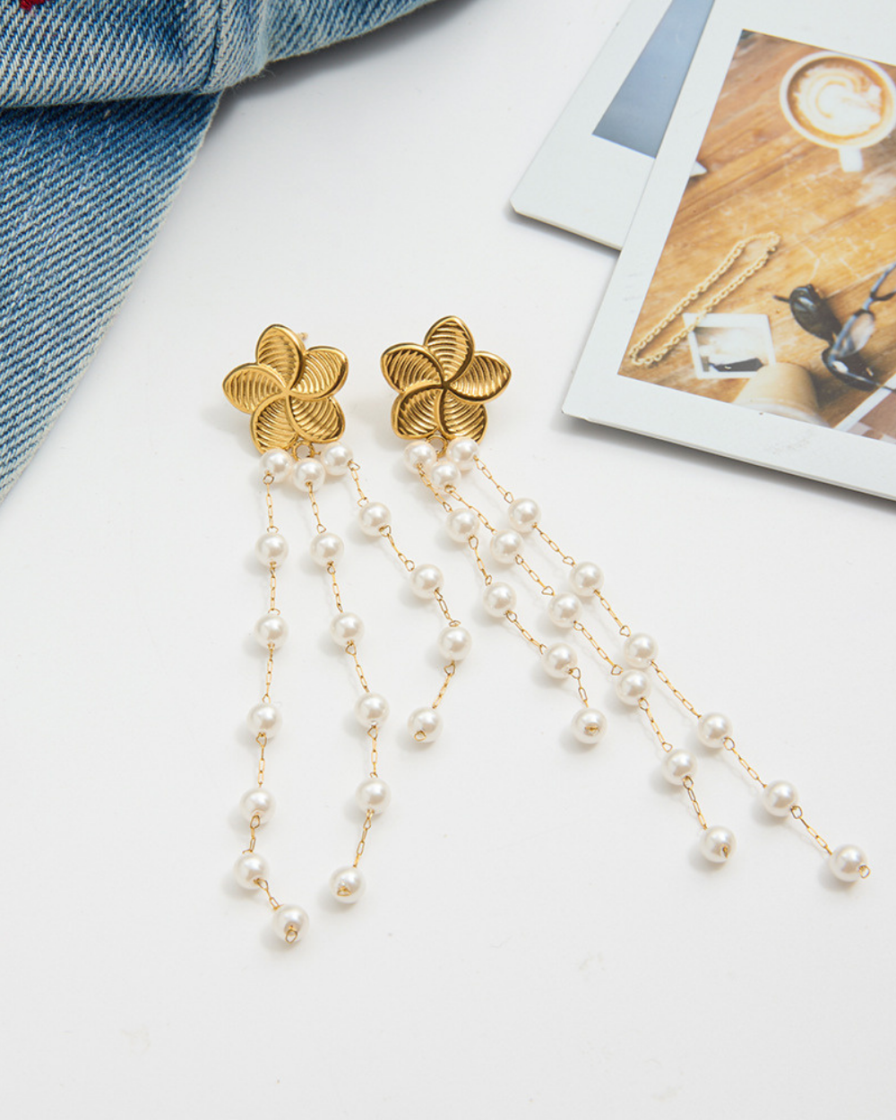 Gold floral earrings with pearl strands on a white surface