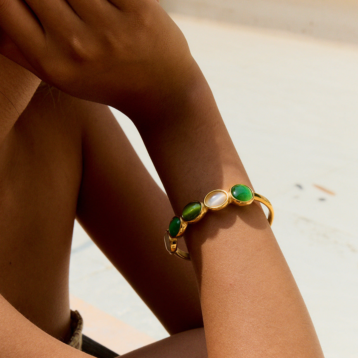 golden open bangle with alternating green and cream stones on wrist under the sun
