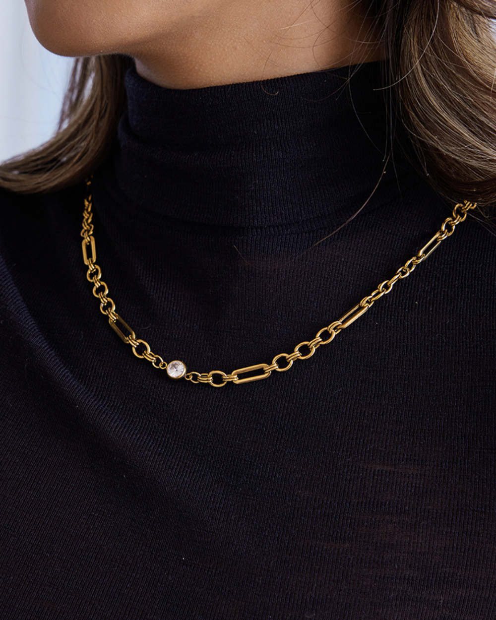 Gold chain necklace with a pearl pendant worn by a person in a black turtleneck.