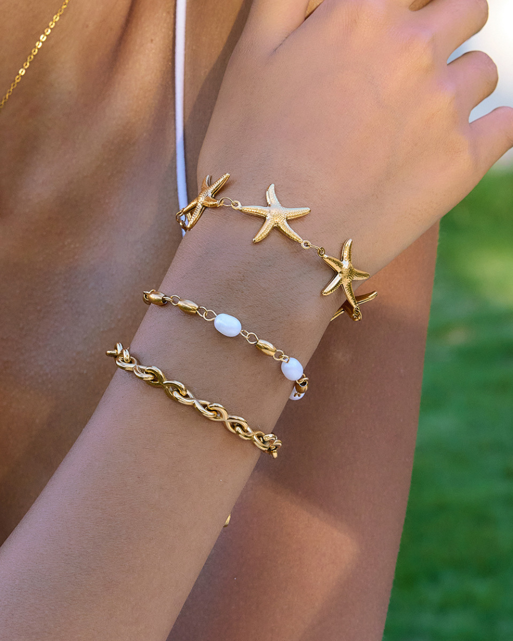 Gold starfish and chain bracelet on a wrist with a blurred green background