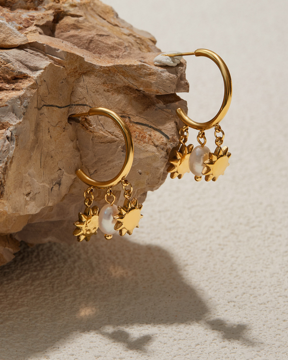 Gold hoop earrings with star-shaped charms on a textured stone surface