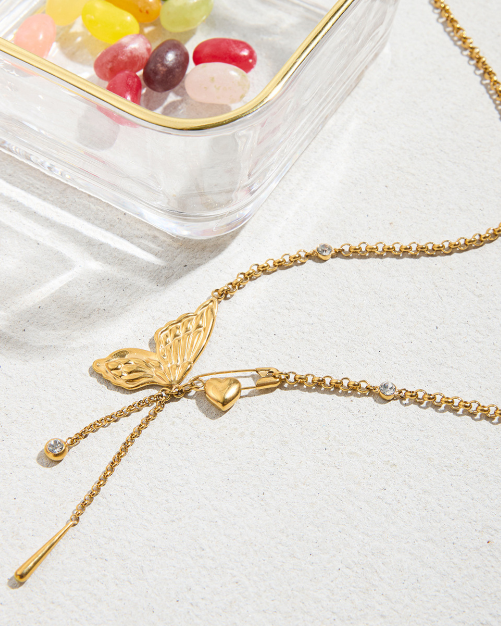 Gold necklace with butterfly and heart charms on a light background