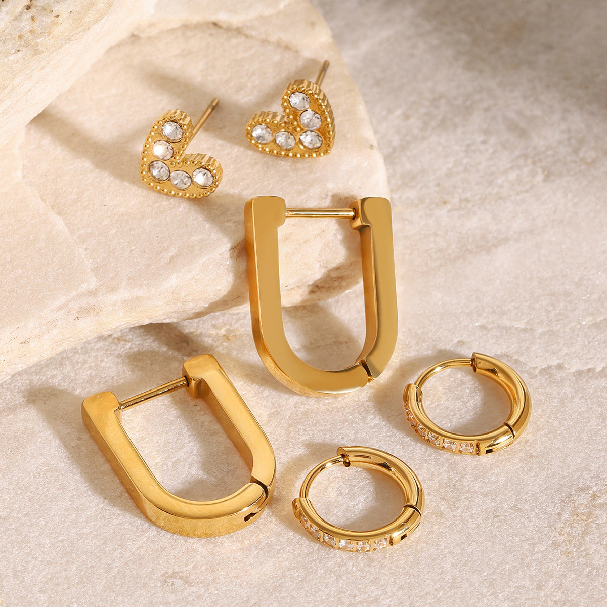 Close-up of gold earrings trio with heart, crystal huggie and bold rectangular hoops