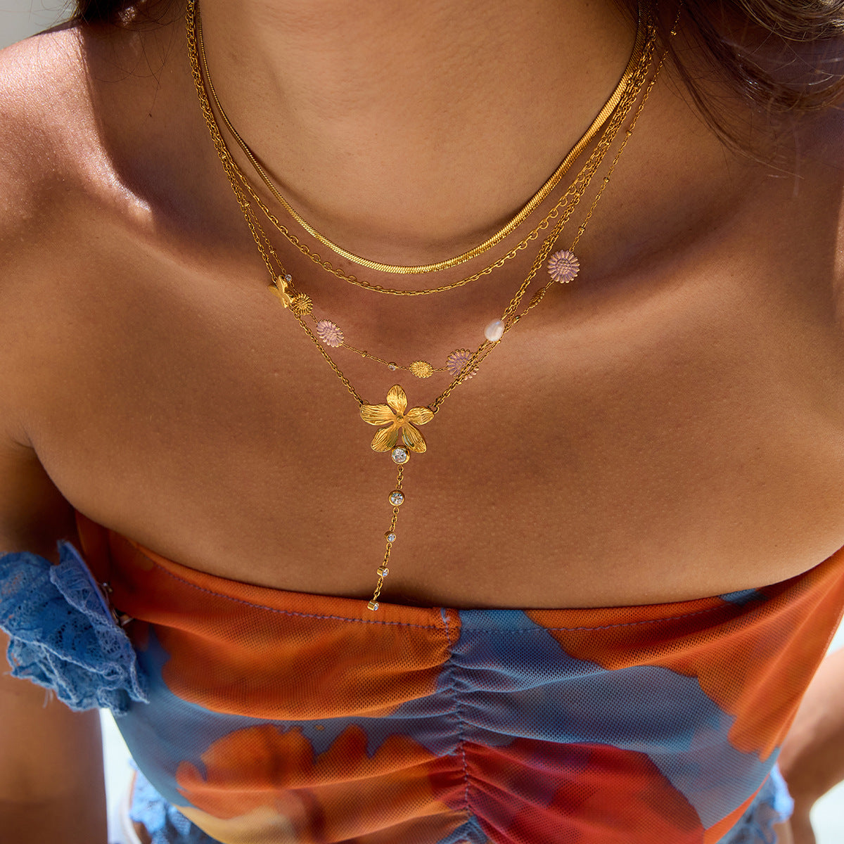 Close-up of a person wearing a gold necklace with floral designs against a blurred background.
