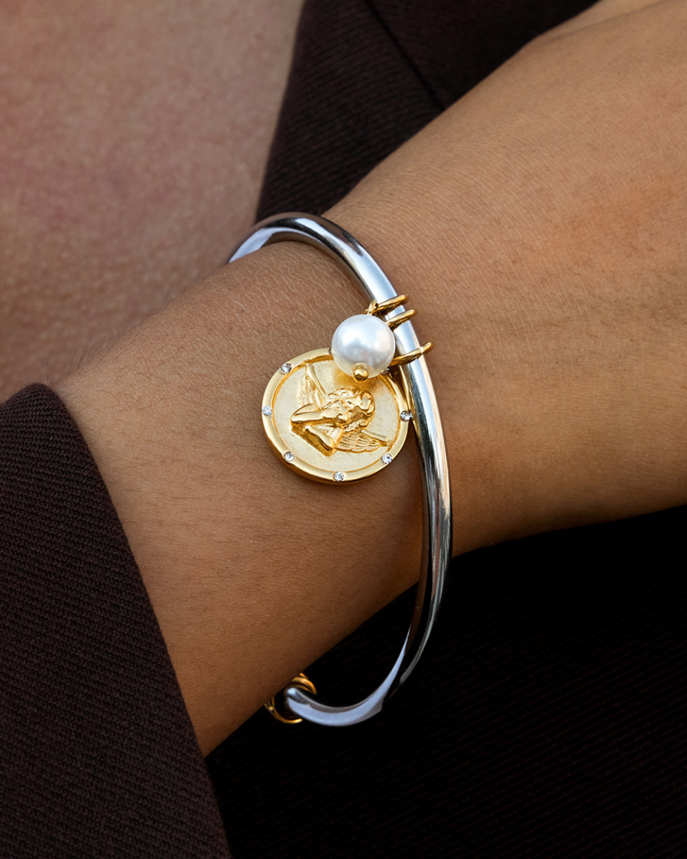 Bracelet with gold coin charm and pearl on wrist against a dark background