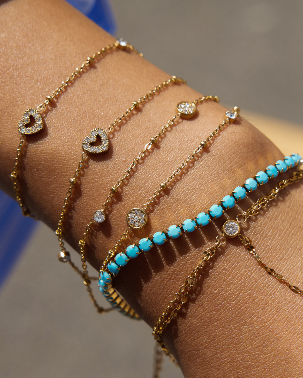 Multiple gold and turquoise beaded bracelets on a wrist against a neutral background