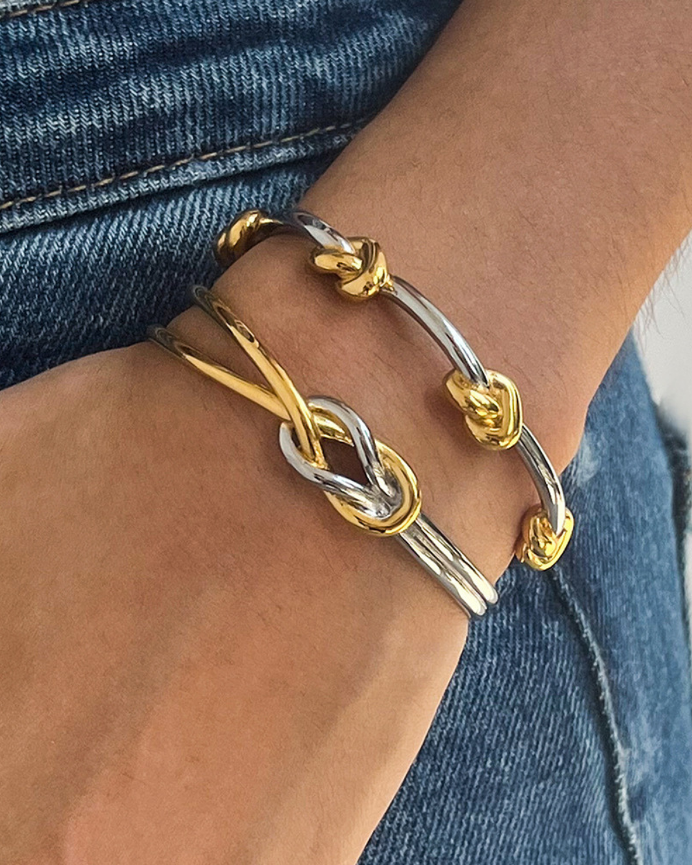 Close-up of a wrist wearing two gold and silver bracelets on a denim background