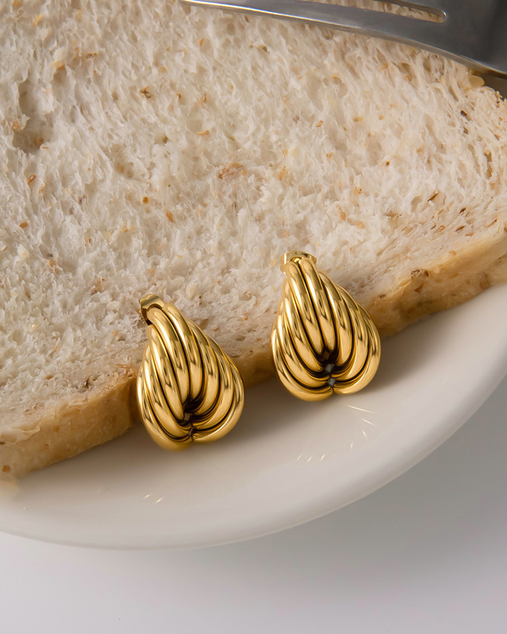Gold earrings on a slice of bread with a knife