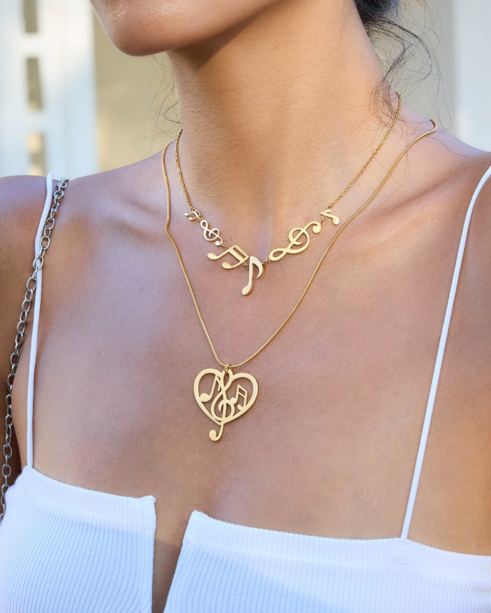 Gold necklaces with musical note designs on a person wearing a white top.