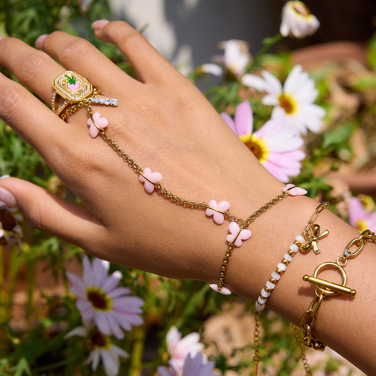 Hand wearing multiple gold bracelets with floral designs against a floral background