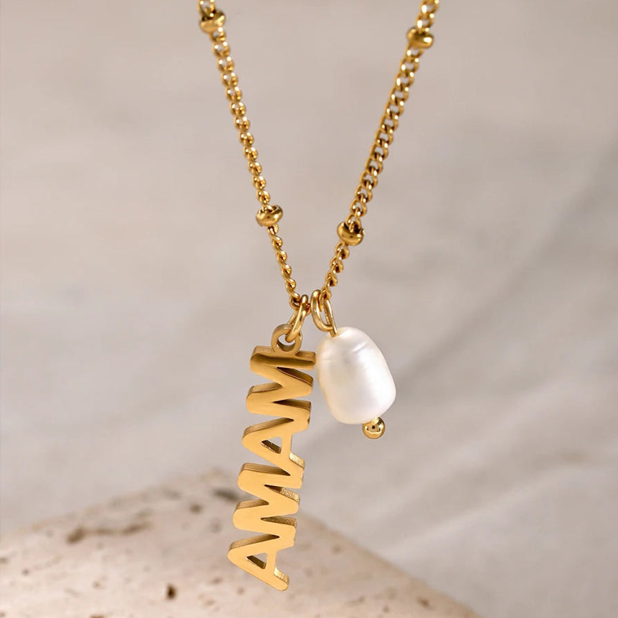 Minimalist gold necklace with MAMA letters and freshwater pearl on white surface