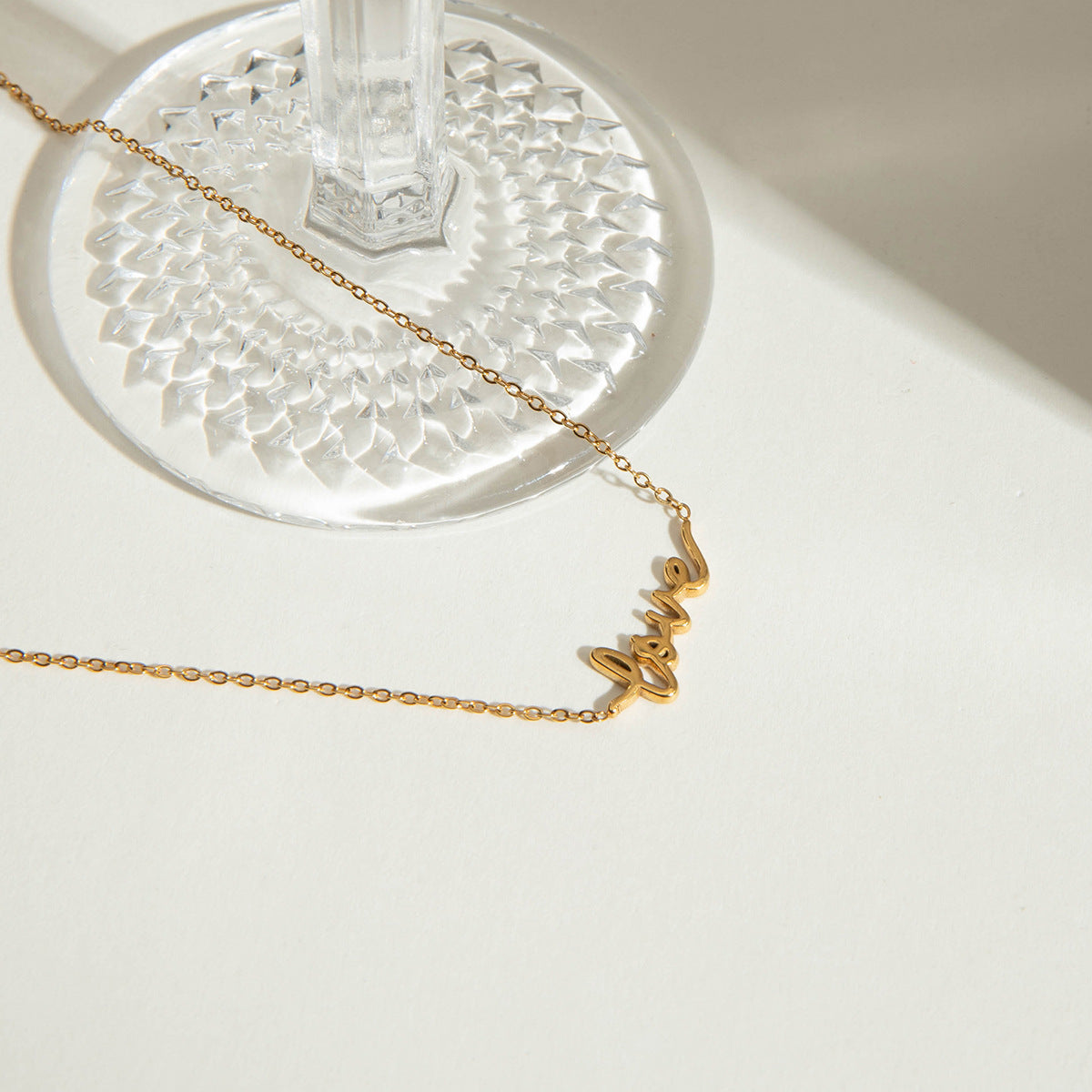 Delicate gold chain necklace spelling "love" next to a glass cup