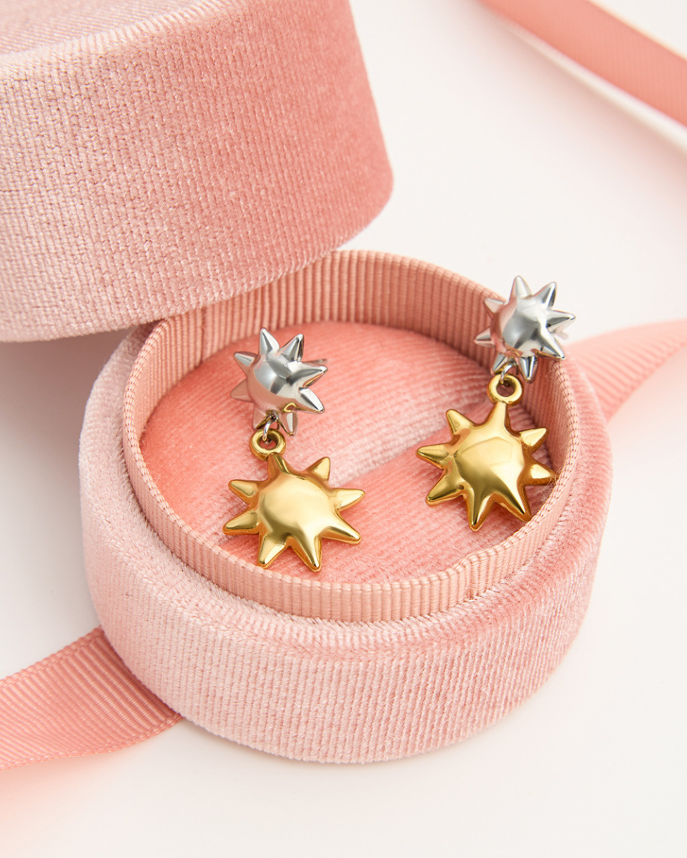 Gold and silver star-shaped earrings on a pink ribbon