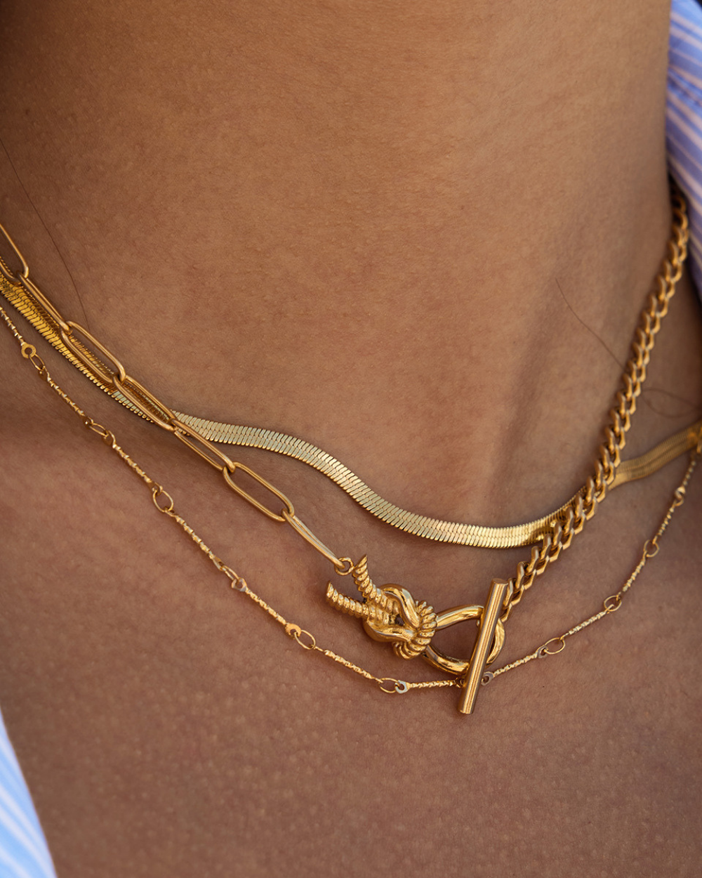 Gold chain necklaces on a person's neck against a brown background