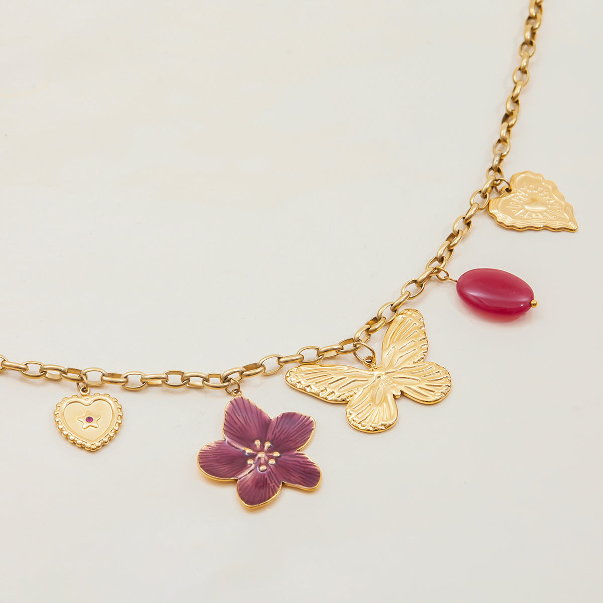 Close-up of gold chain necklace with enamel flower, heart, and butterfly pendants